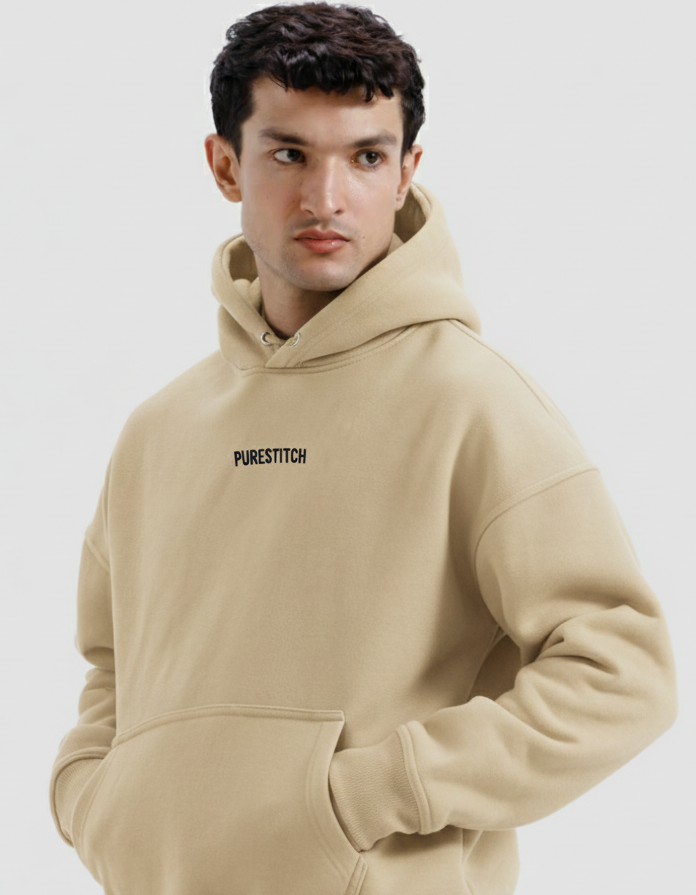 Man wearing a beige hoodie with 'PURESTITCH' branding on a light gray background