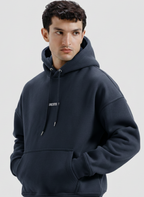 Man wearing a navy hoodie with a brand logo on a light gray background